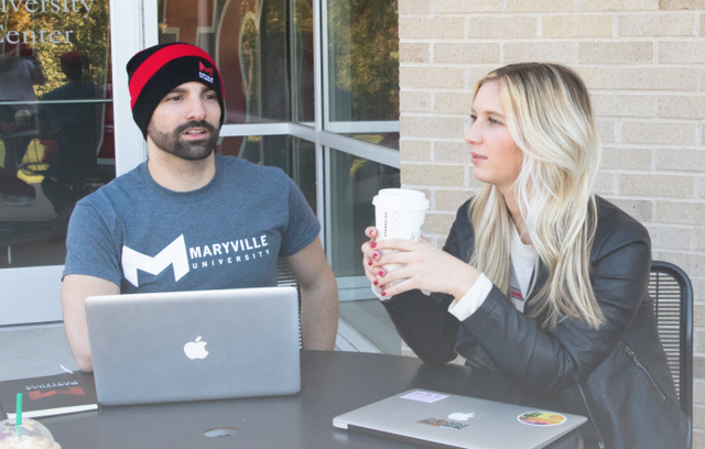Two Maryville students sitting outside at a table drinking coffee and using laptops
